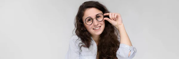 Retrato de uma jovem de óculos. Menina bonita em um fundo cinza. Uma menina em uma blusa leve e calças escuras . — Fotografia de Stock