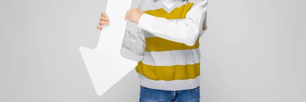 Ein charmanter Junge in weißem Hemd, gestreiftem Tank-Top und heller Jeans steht vor grauem Hintergrund. der Junge hält einen weißen Pfeil in seinen Händen — Stockfoto