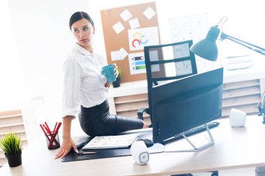 Genç bir kız ofiste bir tabloda bir fincan tutarak ve bir bilgisayar ve belgeleri çalışma oturdu.