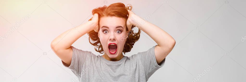 Charming young girl in a gray T-shirt on a gray background. The girl holds her hands behind her head and screams