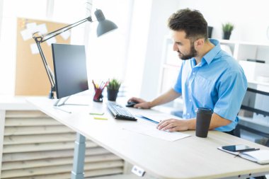 Ofiste ayakta ve bilgisayar masasında çalışan genç bir adam.