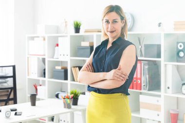 Genç bir kız ofiste standları ve ellerini göğsüne katlanmış.