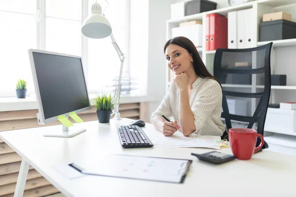 Een jong meisje werken in het kantoor met documenten en een computer. Portret van een jong meisje aan tafel. — Stockfoto