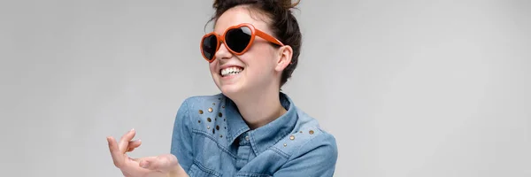 Jonge brunette meisje met bril in de vorm van een hart. De haren worden verzameld in een broodje. Het meisje steekt haar hand. — Stockfoto