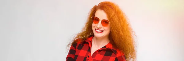 Ritratto di bella rossa felice giovane donna in occhiali da sole sorridente con le mani aperte su sfondo grigio — Foto Stock
