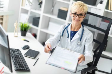 Beyaz bir elbise içinde genç bir kız masada oturur ve ileri bir kalem ve bir belge uzanır.