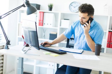 Bilgisayar Resepsiyon ofiste ayakta ve telefonda konuşurken genç bir adam.