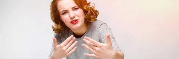 Menina encantadora em uma camiseta cinza em um fundo cinza. A menina estendeu os braços para a frente — Fotografia de Stock