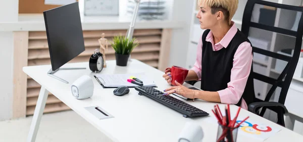 Het meisje werkt op kantoor op de computer en holding een kop. — Stockfoto