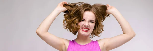 Jovem encantadora em vestido rosa no fundo cinza. Uma menina segura seu cabelo em suas mãos — Fotografia de Stock