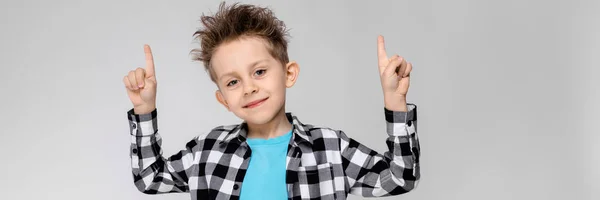 Ein gutaussehender Junge in kariertem Hemd, blauem Hemd und Jeans steht vor grauem Hintergrund. Junge lächelt und zeigt Daumen hoch — Stockfoto