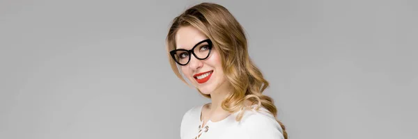 Atractiva joven mujer de negocios rubia en ropa blanca y negra sonriendo sujetando el portapapeles de pie en la oficina sobre fondo gris —  Fotos de Stock