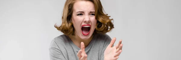 Charmantes junges Mädchen in einem grauen T-Shirt vor grauem Hintergrund. schreit das Mädchen — Stockfoto