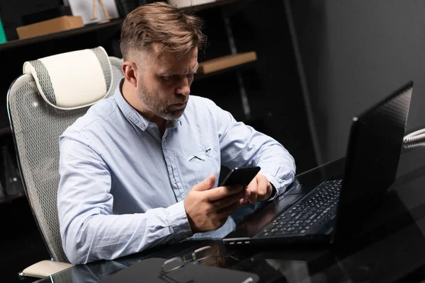 Business man sitting at computer Desk and looking at phone — стоковое фото