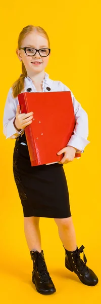 Girl with red hair on a yellow background. A charming girl in transparent glasses is holding a large red folder in her hands. — Stock Photo, Image