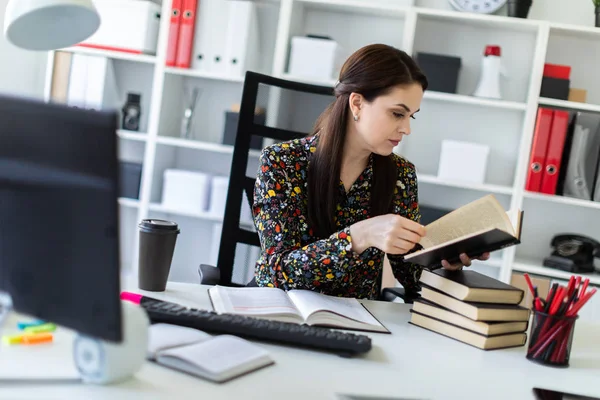 Una joven sentada en la oficina en el escritorio de la computadora y trabajando con un libro . — Foto de Stock