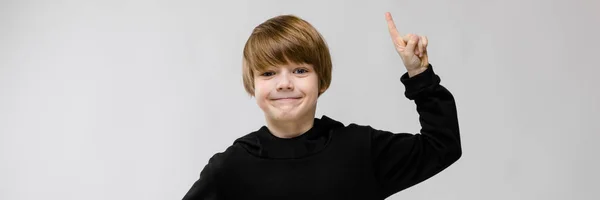 Charmanter Teenager mit blonden Haaren und dunklen Augen. lächelt der Teenager. Ein Teenager zeigt mit dem Finger nach oben. — Stockfoto