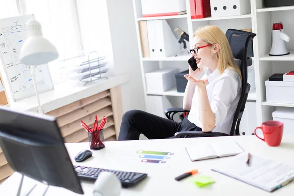 Una joven sentada en la oficina y sosteniendo un teléfono . — Foto de Stock