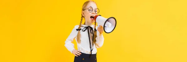 Mädchen mit roten Zöpfen auf gelbem Hintergrund. ein charmantes Mädchen mit runden, transparenten Gläsern schreit in den Lautsprecher. — Stockfoto