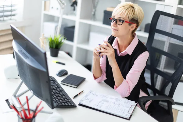 Een jong meisje aan een bureau op kantoor zit en een potlood leunde op haar kin. — Stockfoto