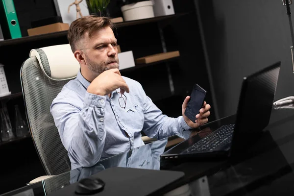 Serious businessman working on a laptop and talking on a mobile phone — Stock Photo, Image