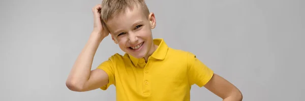 Retrato de lindo niño rubio caucásico en camiseta amarilla pensando en fondo gris — Foto de Stock