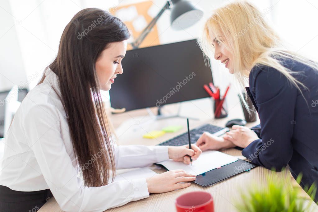 Two girls stand in the office bent over near the table and work with documents.