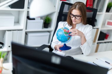 Bilgisayarda ofis masasında oturan ve bir küre tutan genç bir kız.