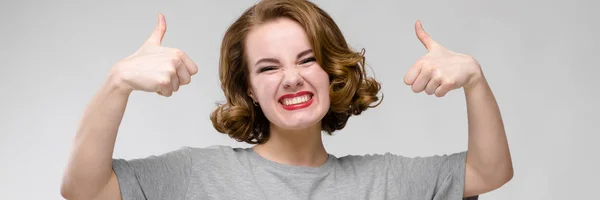 Encantadora joven con una camiseta gris sobre un fondo gris. La chica muestra clase —  Fotos de Stock