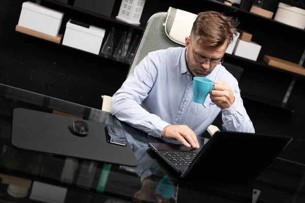 Серьезный бизнесмен работает на ноутбуке и пьет кофе — стоковое фото