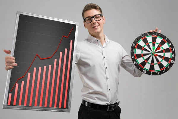 Young man in glasses holding a Board with increasing statistics and Darts isolated on white background — Stock Photo, Image