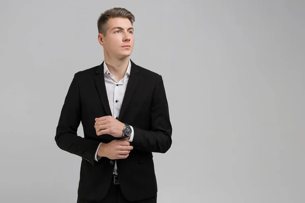 Retrato de hombre joven en traje negro enderezando la manga aislado sobre fondo blanco —  Fotos de Stock