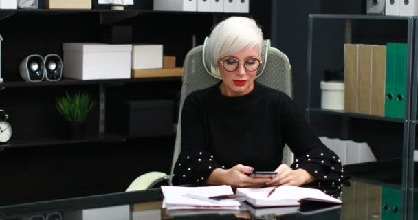 Drukke vrouw praten op de mobiel en landline zittend aan tafel in kantoor — Stockvideo
