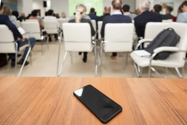 Telefone celular deitado na mesa em primeiro plano no fundo turvo do público na sala de conferências — Fotografia de Stock