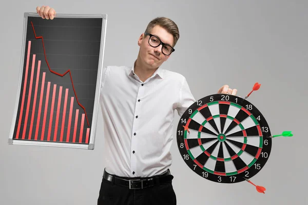 Young man in glasses holding a Board with falling statistics and Darts isolated on white background — Stock Photo, Image