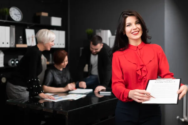 Бізнес-леді з ручкою і контрактом на тлі офісних працівників обговорюють проект — стокове фото