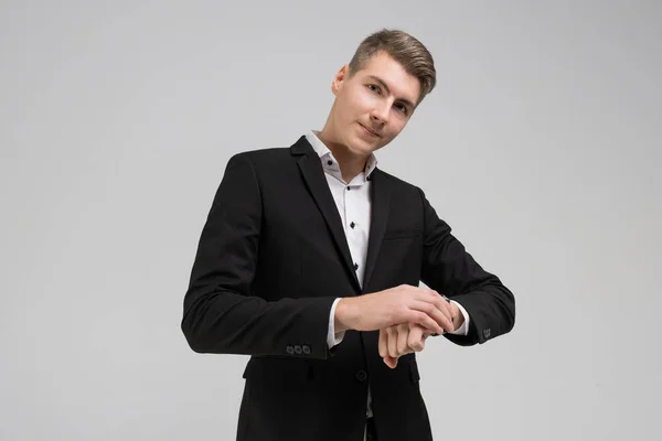 Портрет молодого чоловіка в чорному костюмі випрямляючий годинник ізольований на білому тлі — стокове фото