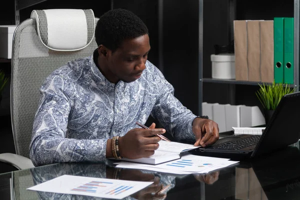 Joven hombre de negocios negro que trabaja con documentos y portátil en la oficina — Foto de Stock