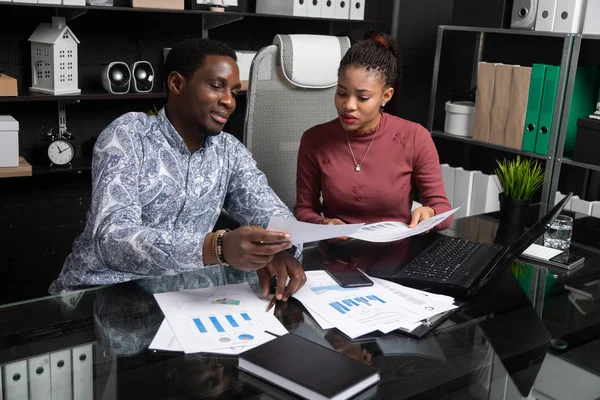 Dos jóvenes negros discuten su negocio usando diagramas sentados en el escritorio de la oficina — Foto de Stock