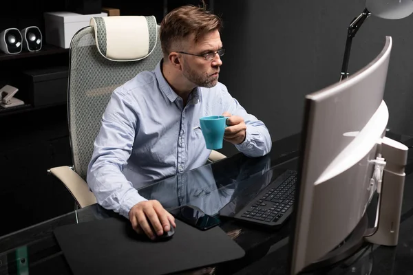 Business man with glasses working in the office at the computer table and drinking coffee from a small Cup — Stock Photo, Image