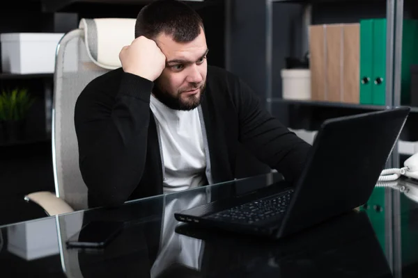 Portrait of young man propping up his head with his fist with laptop in business office — Stock Photo, Image