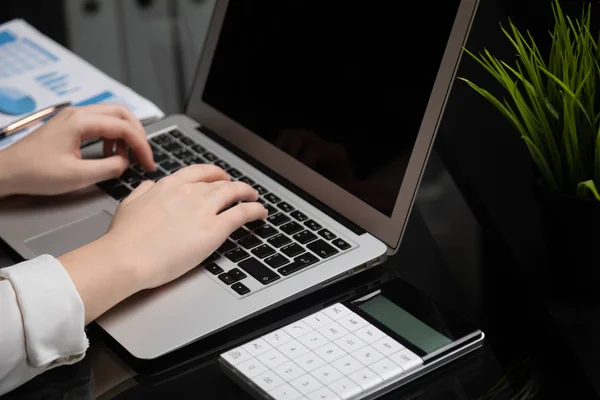 Close-up van de handen typen op laptop met leeg zwart scherm naast grafieken en rekenmachine — Stockfoto