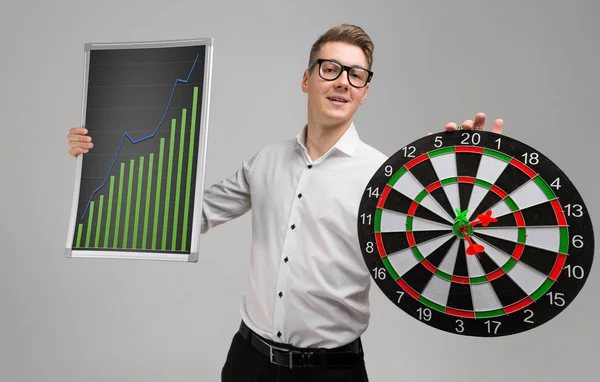 Young man in glasses holding a Board with increasing statistics and Darts isolated on white background — Stock Photo, Image