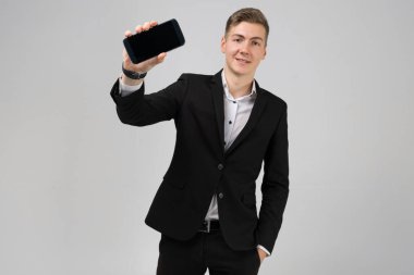 Portrait of young man in black suit shows mobile phone with blank screen isolated on white background