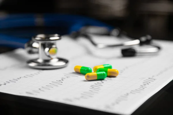 Estetoscópio e comprimidos coloridos deitados na folha com o eletrocardiograma — Fotografia de Stock
