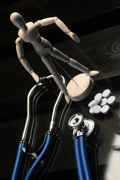 Pills, a stethoscope and a fake person on a black background — Stock Photo, Image
