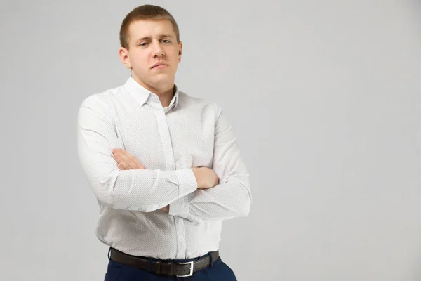 Young man in white shirt stands isolated on white background with folded arms on chest