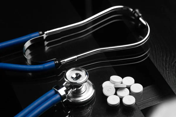 Stetoskop i tabletki są na stole czarny — Zdjęcie stockowe