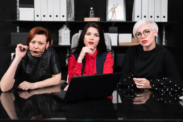 Tres compañeras sentadas en la oficina a la mesa con portátil — Foto de Stock
