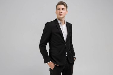 Elleri ceplerinde izole beyaz arka plan üzerinde siyah elbiseli olan genç adam portresi